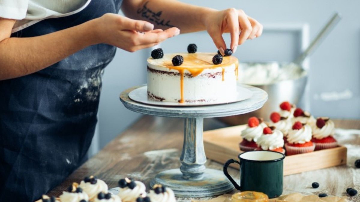 woman decorating a cake with icing and berries